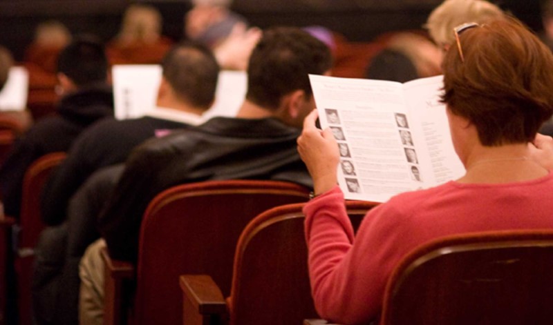 A picture depicting a woman reading opera program notes.